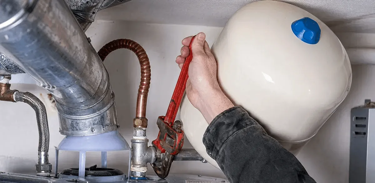 Water heater repair technician tightening plumbing connections near a tank unit in Oakland, CA